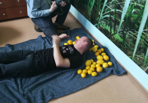 warsztaty fotogtraficzne Rehabilitacja 25 plus Marcin pozuje do zdjęć z cytrynami w pozycji leżącej.